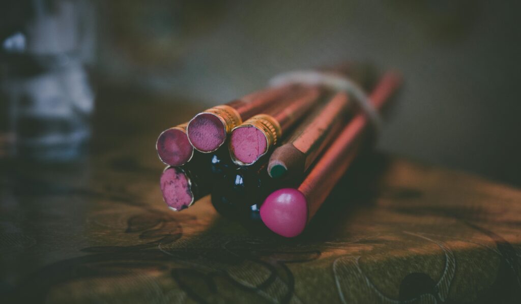 Bundle of colorful pencils with pink erasers on a warm-toned wooden surface.